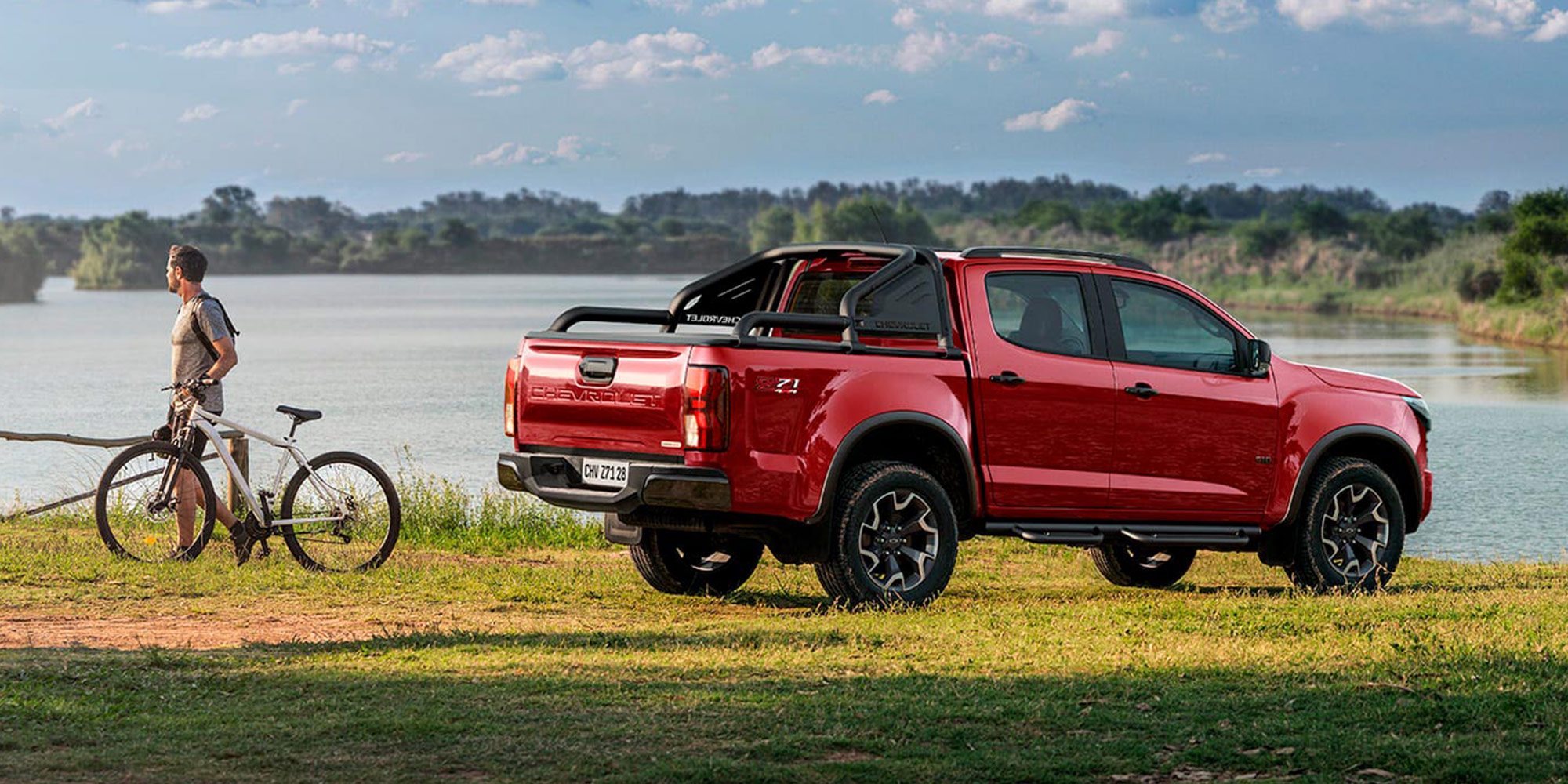 Chevrolet Colorado roja parqueada sobre pasto junto a un lago resaltando su diseño pickup